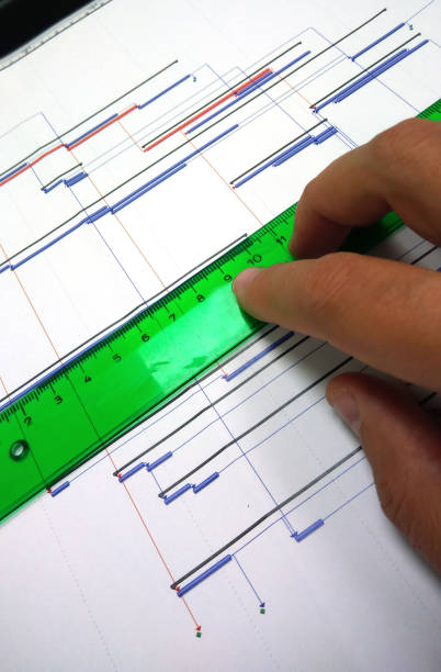engineer working over gantt progress chart of project printed on paper helping himself with green rulen