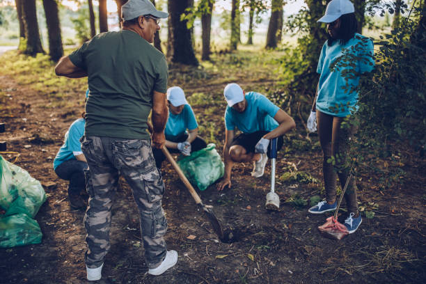 Multi-ethnic group of people, cleaning together in public park, saving the environment, disability man helping them.